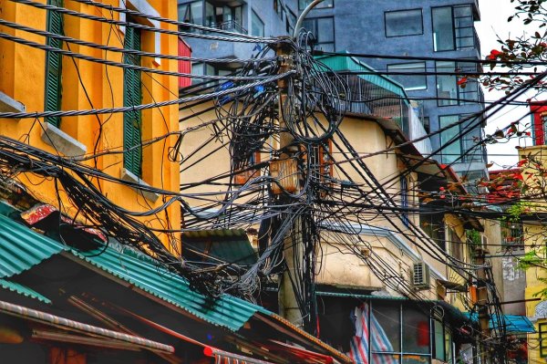 Mast mit vielen durcheinandergehenden Kabeln in einer Stadt