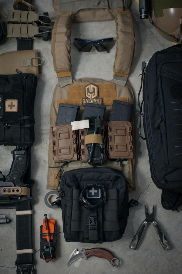 Auf dem Boden liegt eine militärische Kampfausrüstung. Die einzelnen Teile wie Weste, Waffe, Werkzeuge, Helm, Sonnenbrille usw. sind ordentlich nebeneinander gelegt. Das Bild ist eine visuelle Packliste.